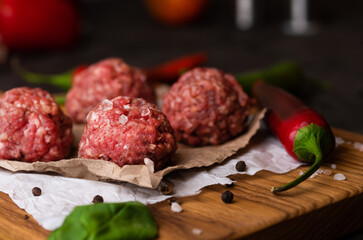 Yummy fresh raw minced uncooked beef meatballs with spinach decoration, black pepper, sea salt on a wooden cutting board. Restaurant cooking food photography.