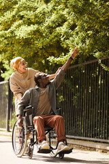 Happy young African-American disabled man in casual outfit reaching to touch leaves while enjoying...