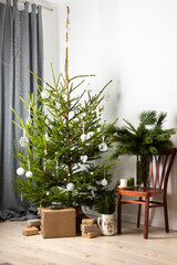 Christmas tree with white toys, old chair with a vase with pine branches, gift boxes under the tree, part of home interior