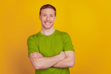 Portrait of attractive man standing with folded arms happy positive smile confident isolated on yellow color background