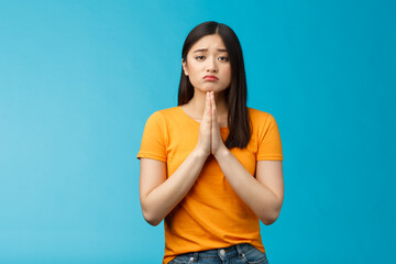 Upset cute silly asian girl praying, plead for help, pouting frowning need, make pitty face, hold...