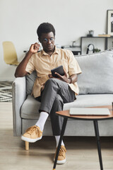 African young man sitting on sofa and using digital tablet during his leisure time at home