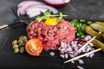 Board with tasty beef tartare on dark background, closeup
