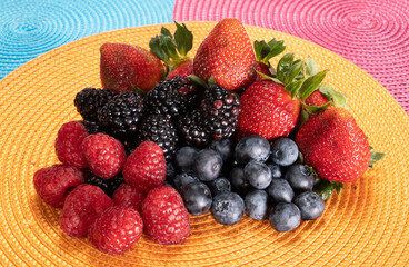 Strawberries, blueberries, raspberries, and blackberries arranged on colorful place mats, mix of delicious berries in a horizontal frame.