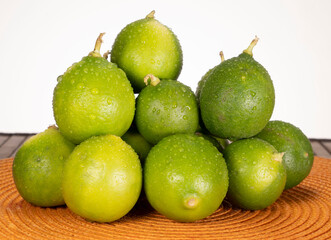 Frontal view of a pile of wet, fresh green Mexican lemons or lime fruit on top of an orange placemat, against a white background, studio shot