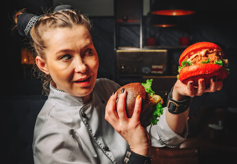 young woman chef with two burger in hands on dark background in cafe