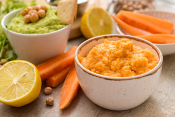 Bowls with tasty carrot hummus, lemon and chickpeas on light background, closeup