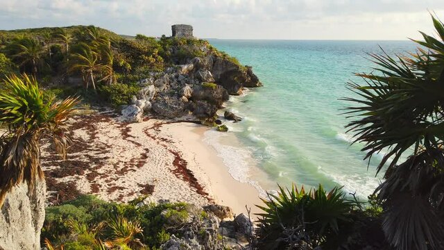 Camera pans up along Tulum's coastline to reveal ancient ruin