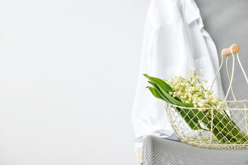 Basket with lily-of-the-valley flowers on chair near light wall