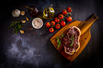 Beef steak on a wooden chopping board with vegetables and spices on black background © Chaded