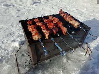 Winter kebabs in nature. Cooking meat in Russian. Pork steaks cooked in the open air in the forest. Meat cooked on fire.