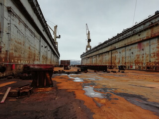 Old rusty floating dry dock. Dry docks are used for the construction, maintenance and repair of ships. Murmansk. Tall cranes are in the working dock.