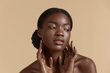 Portrait close up of beautiful african girl. Thoughtful young woman touch her clean face. Concept of face skin care. Isolated on beige background. Studio shoot