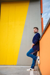 a man in a blue jacket and jeans is pensive and serious, stands against the background of a yellow wall