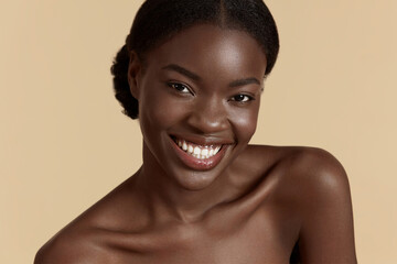 Portrait close up of beautiful african girl. Smiling young woman looking at camera. Concept of skincare. Isolated on beige background. Studio shoot