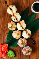 japanese sushi rolls with cheese cap and roll with raw salmon and tuna in a restaurant serving on a wooden board on a dark background. top view.