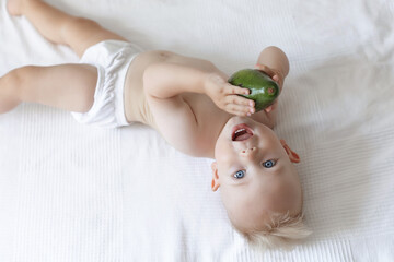 small cute child lying on the bed and holding an avocado in his hands