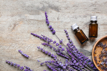 Bottles of lavender essential oil and flowers on wooden background