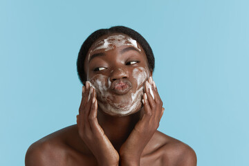 Close up portrait of beautiful black girl wash her face with cleansing face foam. Smiling young...