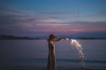 Fototapeta premium 夕暮れの海で花火をする女性