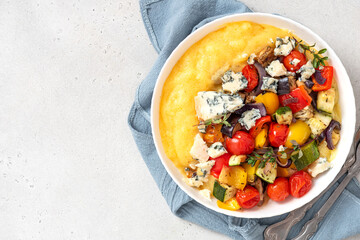 Polenta with stewed vegetables and herbs in a bowl on a white background. Top view. Polenta with tomatoes, peppers, zucchini, eggplant and thyme. Italian cuisine, vegetarian food. Free space for text