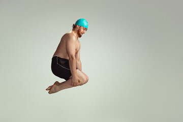 Funny dive. Cute red-headed man in red swimming shorts posing isolated on gray studio background....