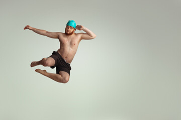 Funny dive. Cute red-headed man in red swimming shorts posing isolated on gray studio background....