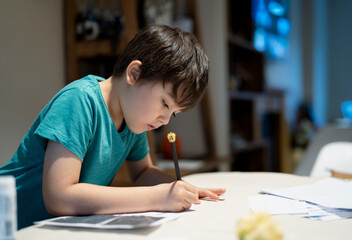 Portrait of school kid siting on table doing homework, Child boy holding pencil writing on paper, Homeschooling , back to school concept