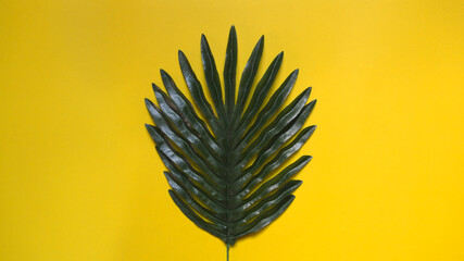 Fototapeta na wymiar Plastic fake palm leaves placed in center of photo on yellow paper background, minimalist concept.