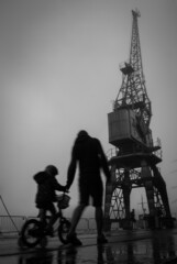Silhouette of mother and child on bike at bristol docks, with crane in background