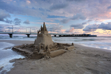 Zamek z piasku na plaży w Kołobrzegu, w pięknych barwach wschodzącego słońca. - obrazy, fototapety, plakaty