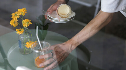 selective focus Staff cleaning coffee shop tables cafe Cake plates and drink restaurant table decorated with yellow flowers in clear glass vases. small coffee shop in Thailand