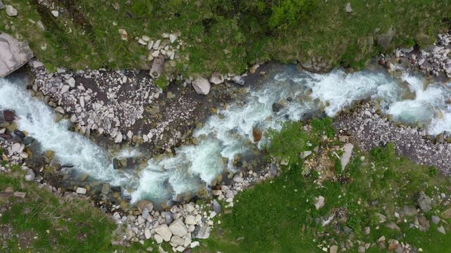 Top Down view of Fast Moving Mountain River with Rapids. Aerial View of Natural Winding River in Green grass field