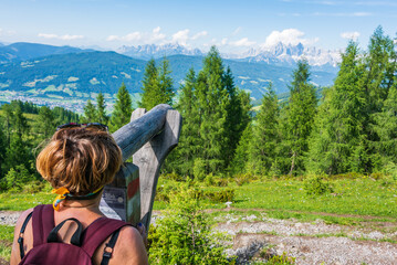 Naklejka premium A tourist on a mountain trail, watching through a wooden telescope the Hoher Dachstein and massif Dachstein. Mountains peaks covered with clouds. Upper Austria-Styria, Austria