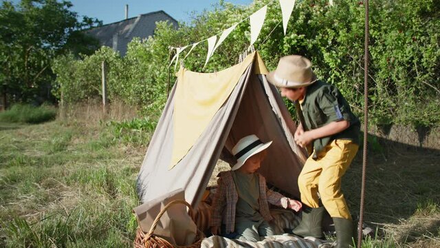 summer vacation, joyful male children have fun building wigwam on green lawn while relaxing in village
