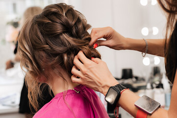 Naklejka premium A girl-hairdresser makes a client's hairstyle for the celebration by pinning the strands with hairpins and hairpins.