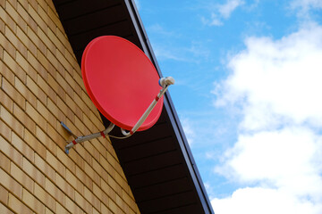 Satellite antenna of red color against  background of  roof of  brick house and  blue sky