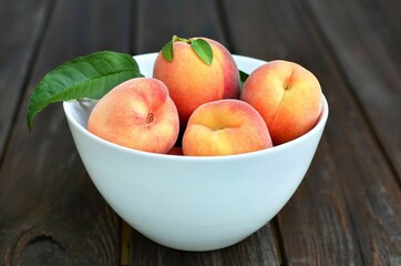 White bowl with ripe peach fruits on a rustic wooden table. Healthy eating concept.