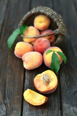 Close-up of fresh juicy ripe peaches scattered next to a wicker basket on an old wooden table, selective focus at the bottom of the image. Healthy eating concept.