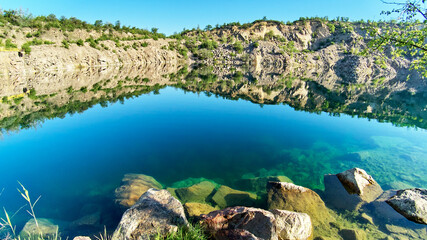 Mountain lake in the summer. Panoramic view on old flooded granite quarry with radon water. Landscape with rock stones, green trees and clean pond