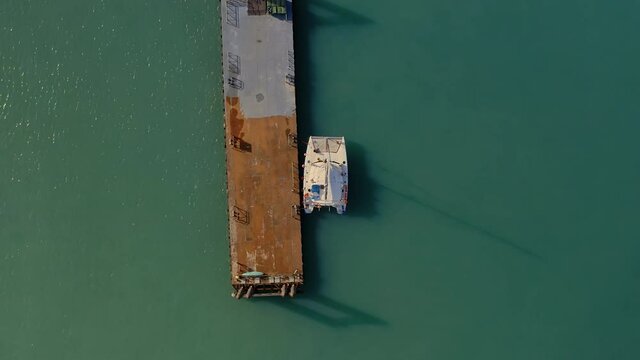 A catamaran with tourists is parked at the pier. Tourists in orange life jackets on a boat trip. The travel business is recovering from the coronavirus pandemic. Drone video top down bird eye view.