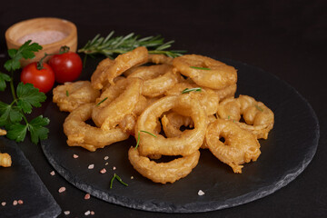 Homemade baked onion rings fries with mayonnaise, Tomato sauce and rosemary on stone board. fast food products : onion rings on cutting board, on black stone background, unhealthy food.