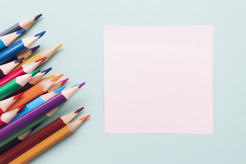 Colored pencils and a sheet for notes lie on a blue background. Top view. Background to-do list...