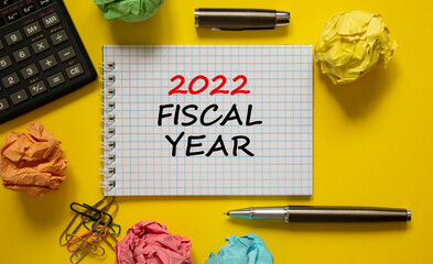 2022 fiscal new year symbol. White note, words 2022 fiscal year on beautiful yellow table, colored paper, colored pencils, paper clips, coins, calculator. Business and 2022 fiscal new year concept.