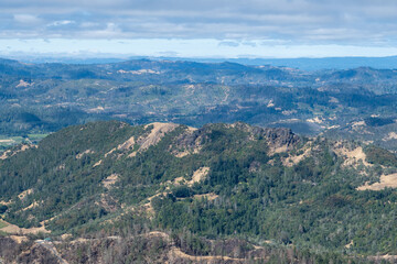 Fototapeta na wymiar Overview of the Napa Valley from the Table Rock Trail, Robert Louis Stevenson State Park on a partly cloudy day with blue sky, featuring a green forest 