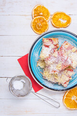 Strawberry souffle cake on blue plate and wheels of dried orange, eggshells on white wooden desk, view from the top. Vertical photo.