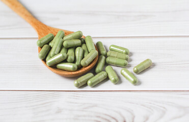 Andrographis paniculata capsule in wooden spoon on wooden background., Herbal extract medicine tablets pills.