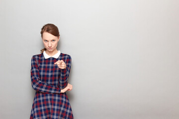 Portrait of serious young woman pointing with index finger at you
