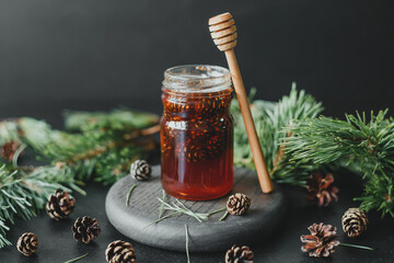 Pine cone jam in a glass jar, against the background of pine branches and cones.