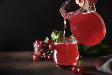 Pouring red cherry compote in glass on dark table. Space for text.